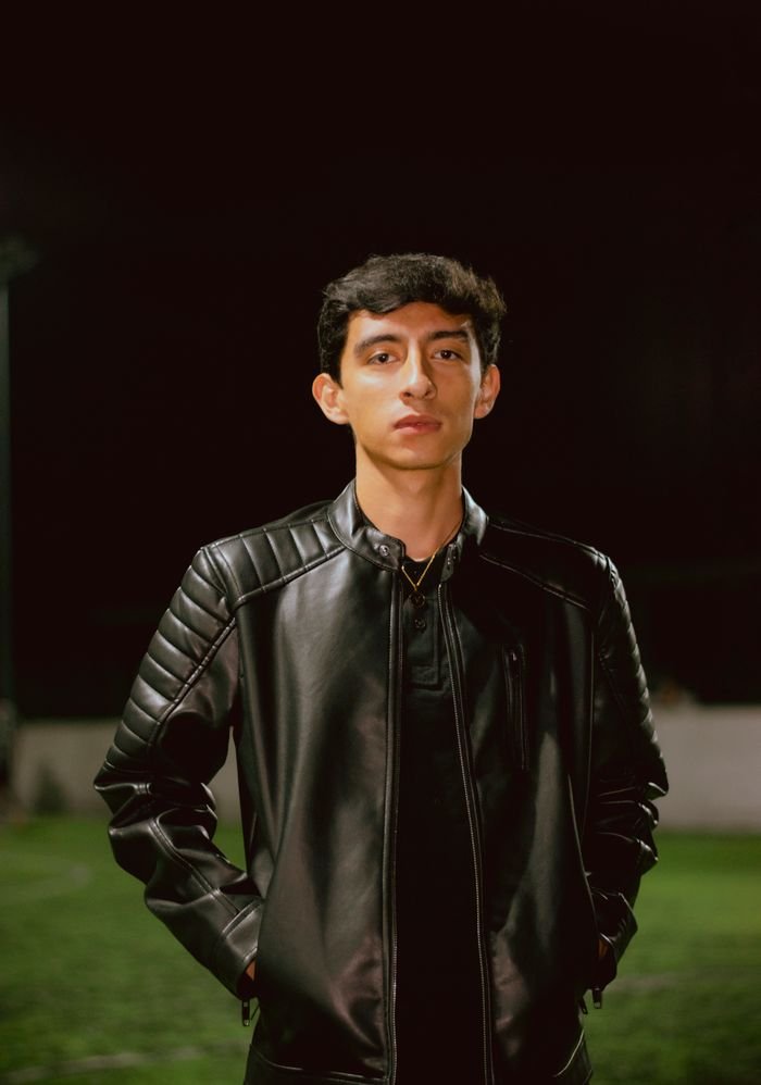 A young adult wearing a black leather jacket standing outdoors at night.