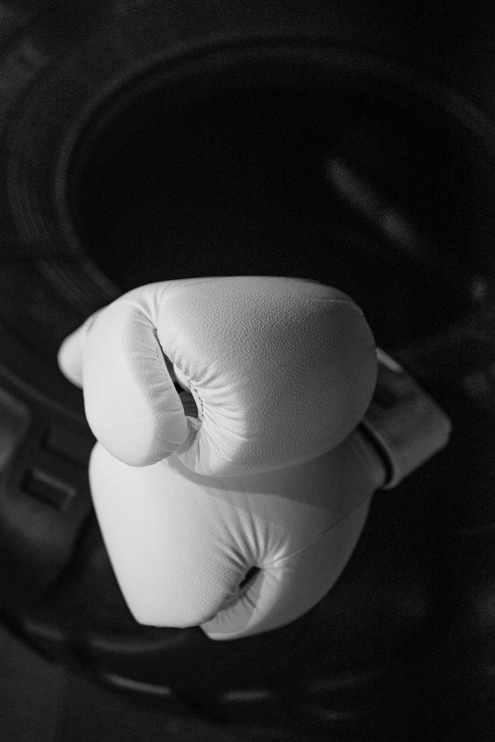 Monochrome image showcasing a pair of white boxing gloves resting on a tire.
